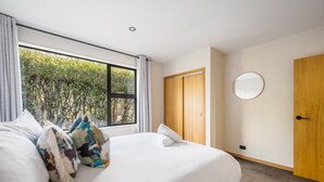 Een hotelkamer met een groot bed, een houten garderobe, een ronde spiegel en een raam met uitzicht op groen.