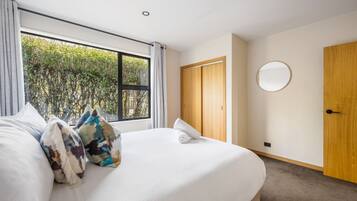 Ein Hotelzimmer mit einem großen Bett, einem Holzschrank, einem runden Spiegel und einem Fenster mit Blick auf Grünflächen.