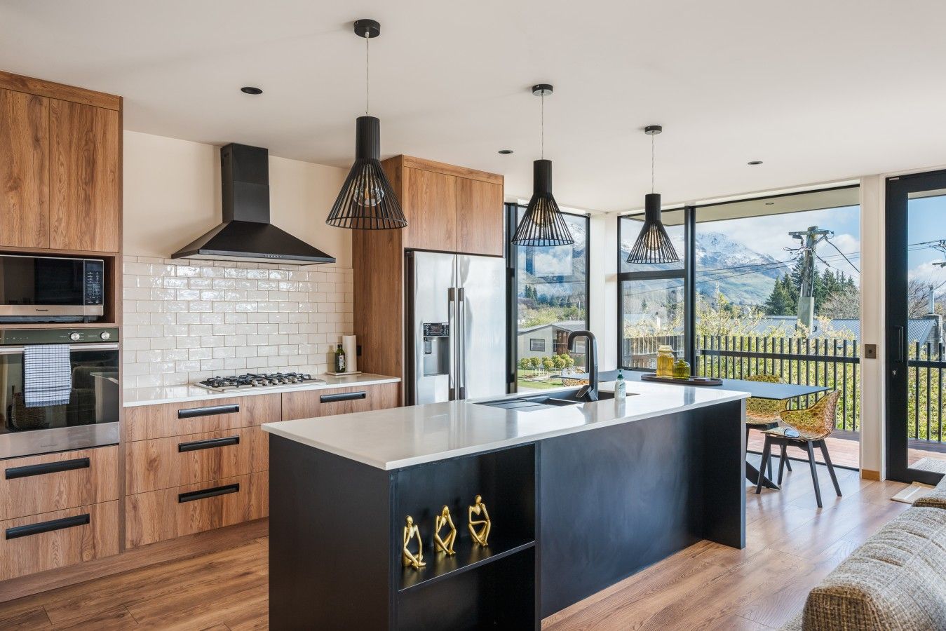 A modern kitchen with wooden cabinets, a black island, and pendant lights.