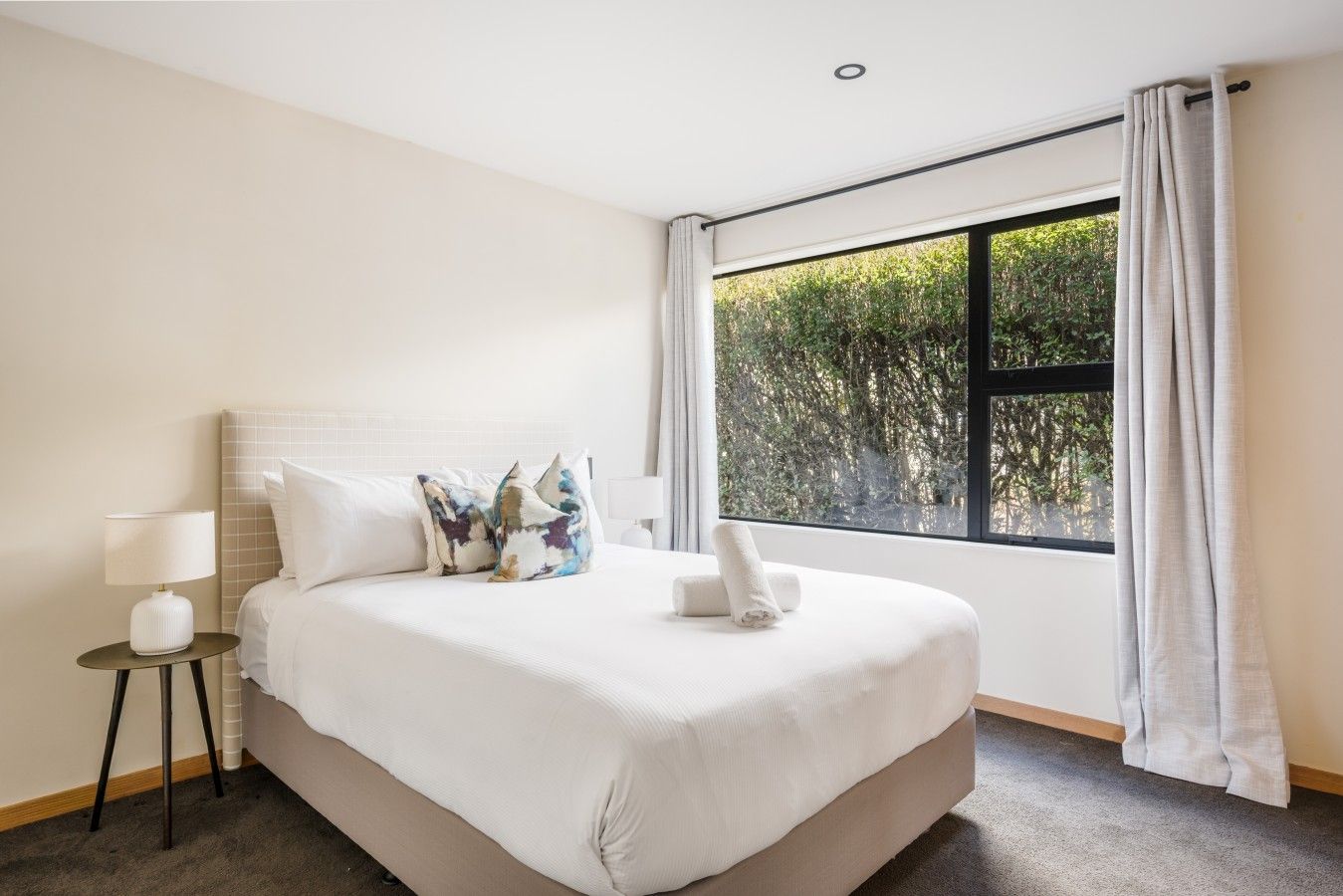 A hotel room with a bed, a nightstand, a lamp, and a window with curtains.