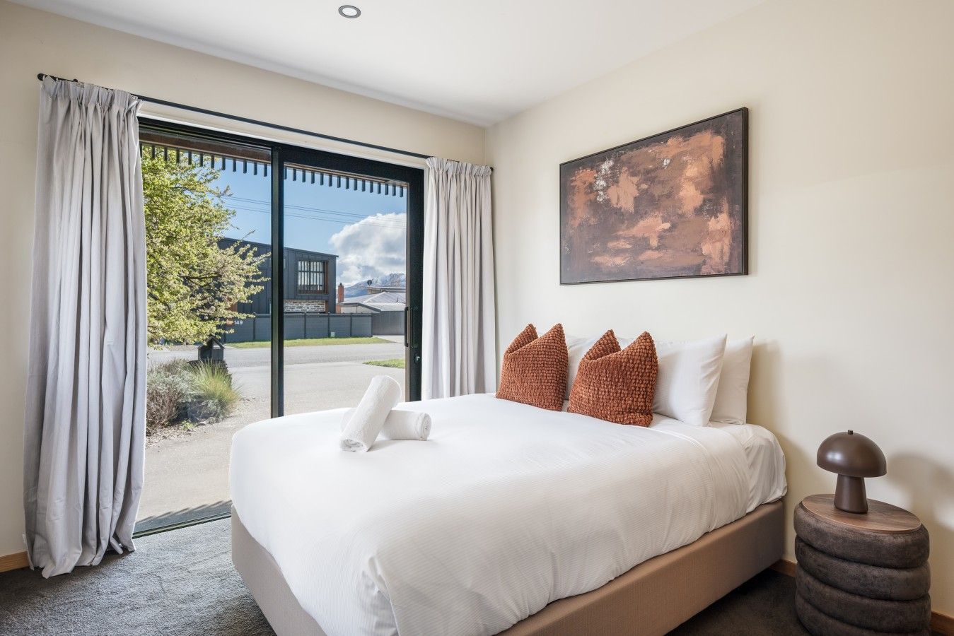 Ein Hotelzimmer mit einem großen Bett, einem Gemälde an der Wand und Blick durch die Glastür.