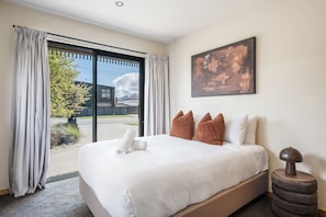 Une chambre d’hôtel avec un grand lit, un tableau au mur et une vue à travers la porte vitrée.