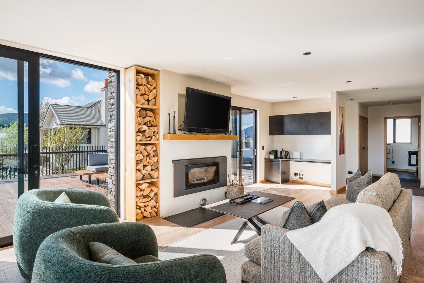 Ein modernes Wohnzimmer mit Kamin, Flachbildfernseher und einem Balkon mit Blick auf ein Haus und Bäume.