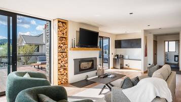 Ein modernes Wohnzimmer mit Kamin, Flachbildfernseher und einem Balkon mit Blick auf ein Haus und Bäume.
