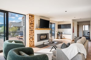 Un salon moderne doté d’une cheminée, d’un téléviseur à écran plat et d’un balcon offrant une vue sur une maison et des arbres.
