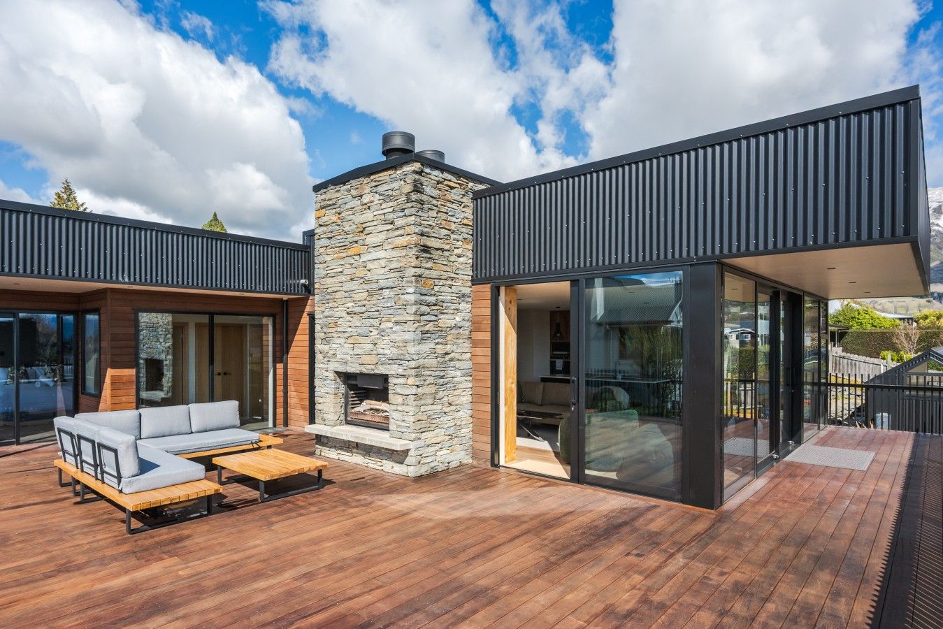 A modern outdoor deck with a stone fireplace, a wooden bench, and a sofa.