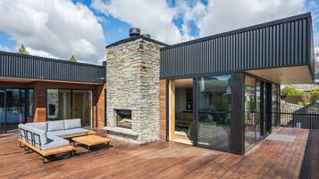 A modern outdoor deck with a stone fireplace, a wooden bench, and a sofa.