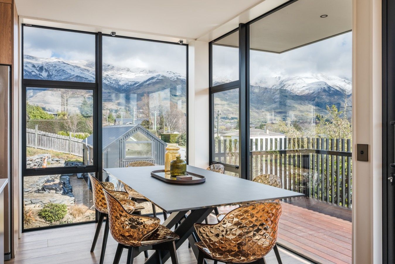 Ein Essbereich mit Tisch und Stühlen, großen Fenstern mit Blick auf die Berge und einer Holzterrasse draußen.