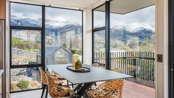 Ein Essbereich mit Tisch und Stühlen, großen Fenstern mit Blick auf die Berge und einer Holzterrasse draußen.