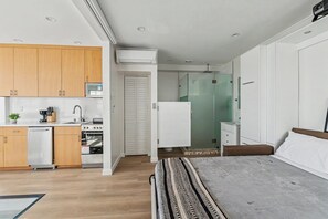 A modern bedroom with a large bed, a small kitchenette, and a bathroom with a glass shower. - Ocean Front Boardwalk Nest with Direct Beach Access (Santa Monica)