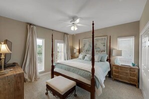 Une chambre à coucher avec un lit à baldaquin, un ventilateur de plafond, une table de chevet avec une lampe, une commode et une fenêtre avec des stores.