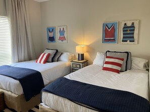 Una camera d'albergo con due letti, un comodino con una lampada e un quadro raffigurante abiti.