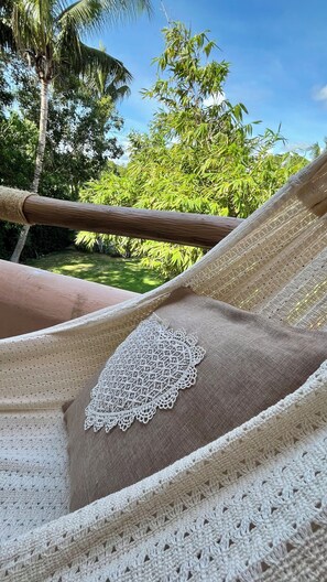 A hammock with a white crocheted pillow, set against a backdrop of lush greenery and a clear sky.