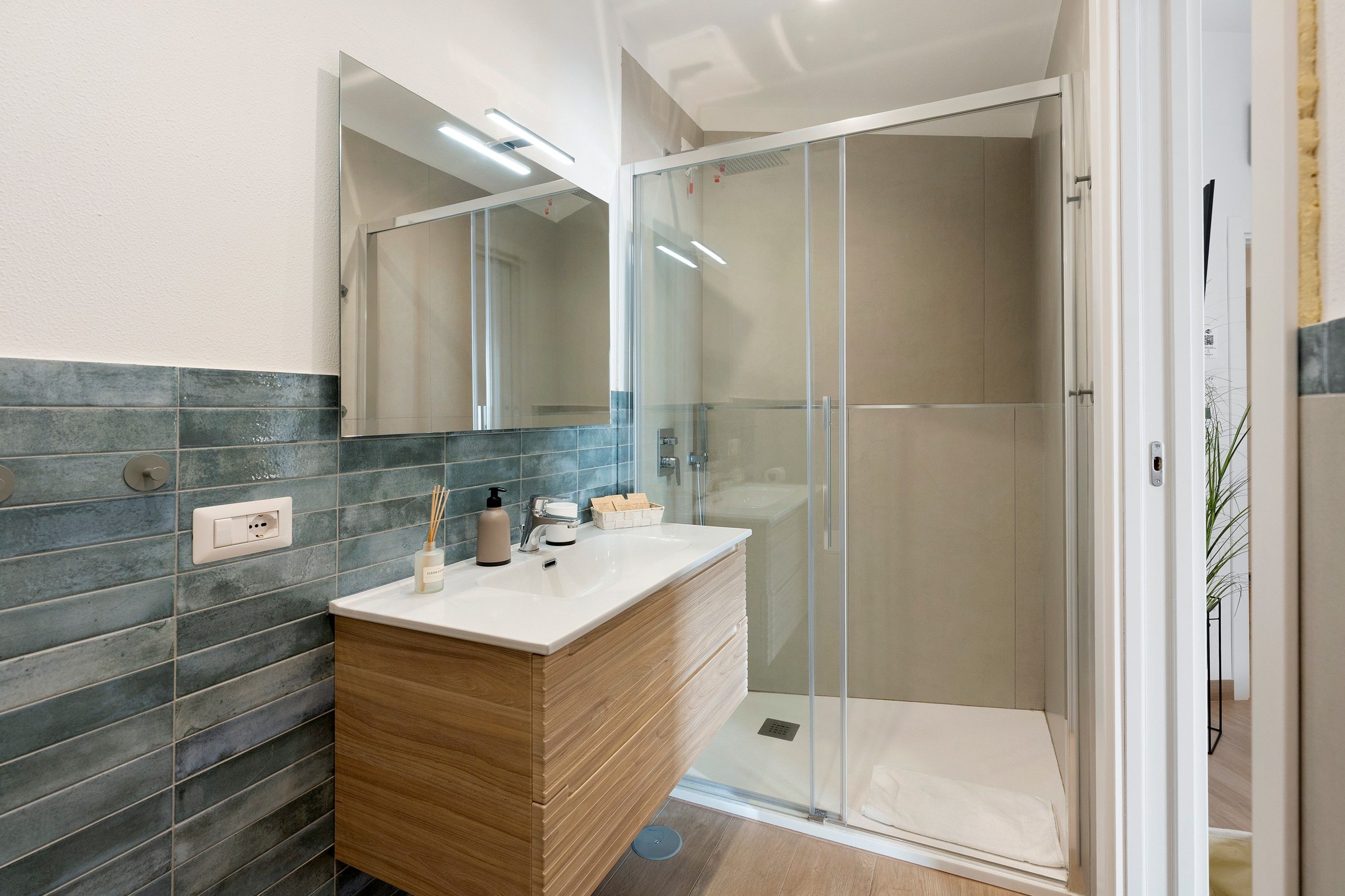 A modern bathroom with a glass shower enclosure, a wooden vanity, and a large mirror.