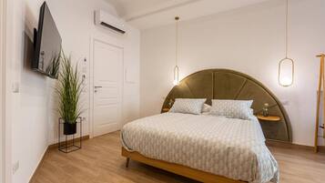 A bedroom with a bed, a television mounted on the wall, an air conditioning unit, and a potted plant.
