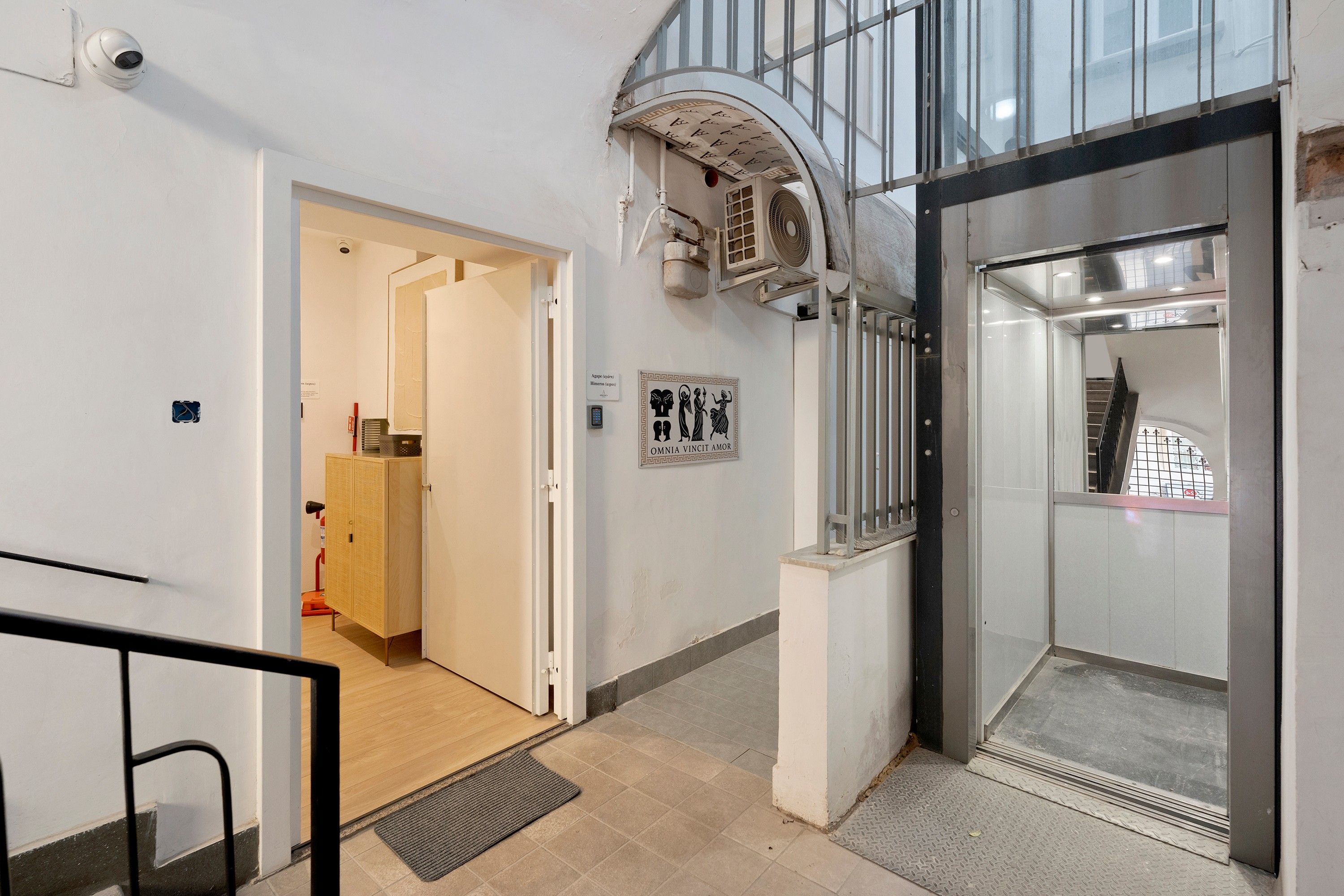 En modern interiör med en glashiss, en dörr med övervakningskamera och en väggmonterad skylt.
