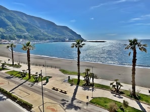 Una strada costiera con palme, una spiaggia e una montagna sullo sfondo.
