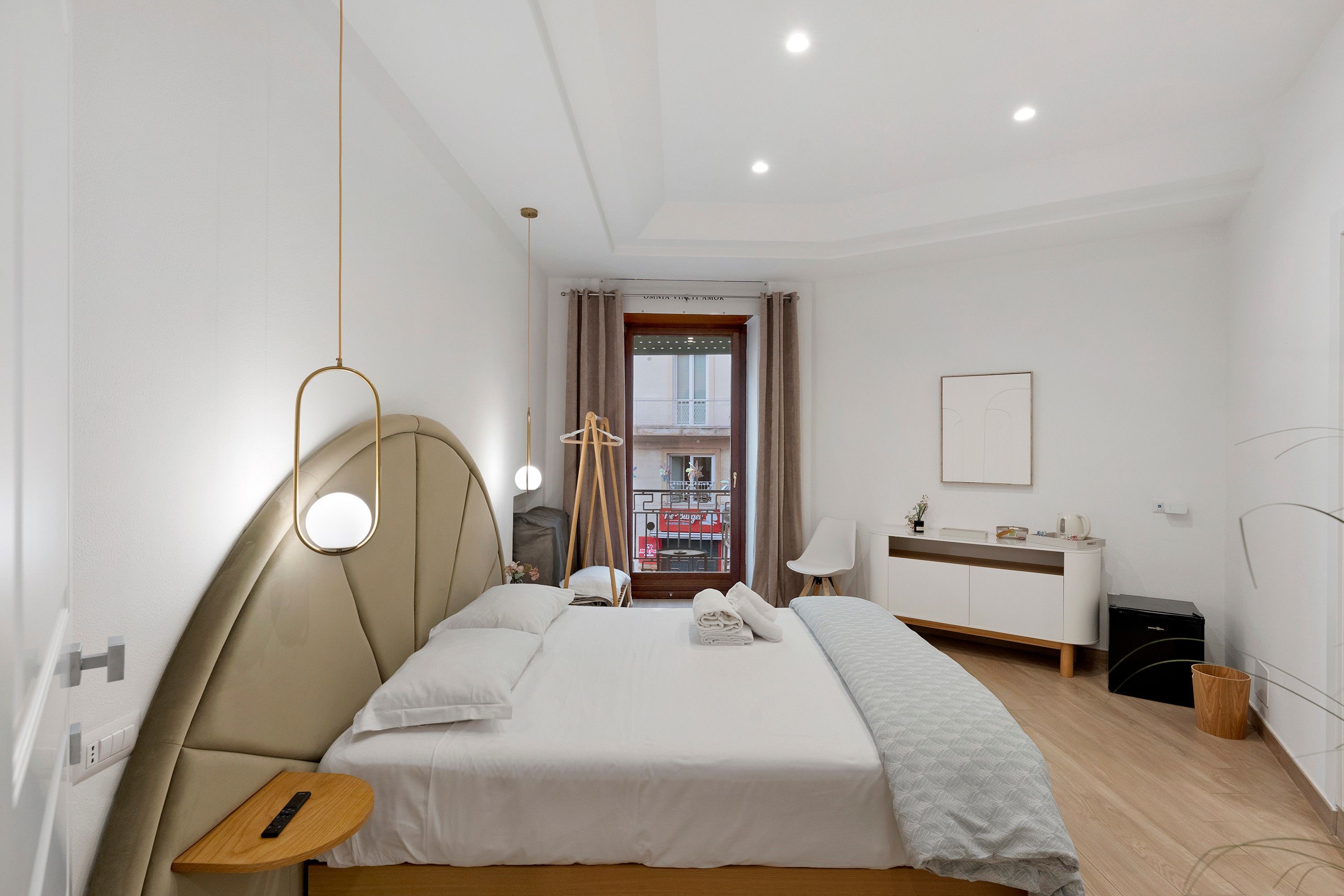 Een hotelkamer met een bed, nachtkastje, lamp en uitzicht op de straat.