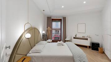 Een hotelkamer met een bed, nachtkastje, lamp en uitzicht op de straat.