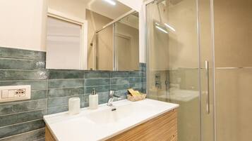 Un bagno con un lavandino bianco, uno specchio e un box doccia.