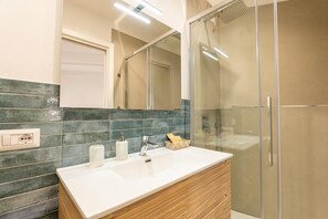 Un bagno con un lavandino bianco, uno specchio e un box doccia.