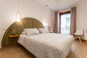Una camera da letto moderna con una testiera curva, un letto con copripiumino fantasia, comodini, una lampada a sospensione e vista all'esterno attraverso una finestra con tende.