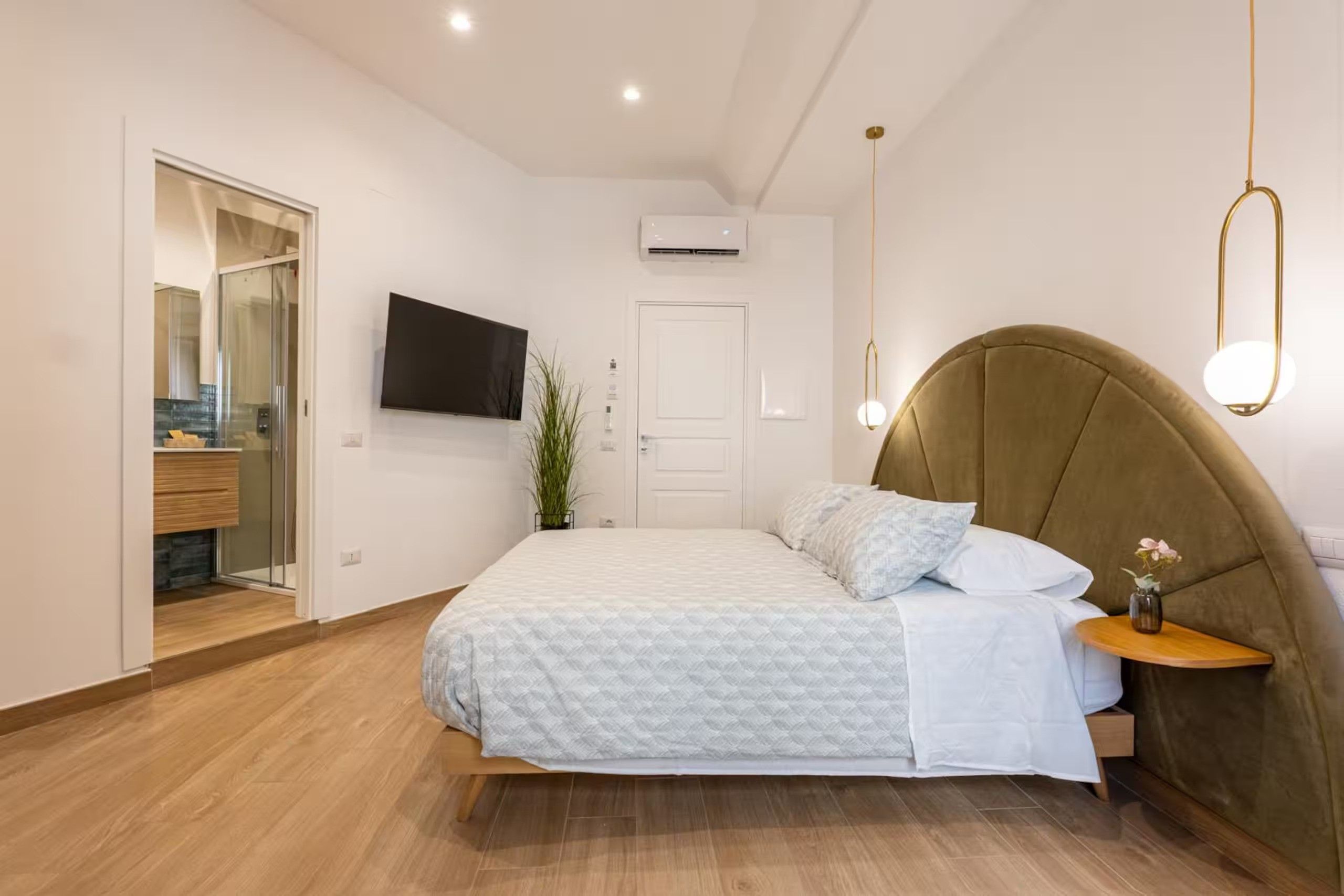 Una camera da letto con un letto, un comodino, una TV a parete e un'anta che dà sul bagno.