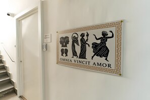 Un corridoio con un cartello a parete raffigurante figure classiche e la frase 'OMNIA VINCIT AMOR'.