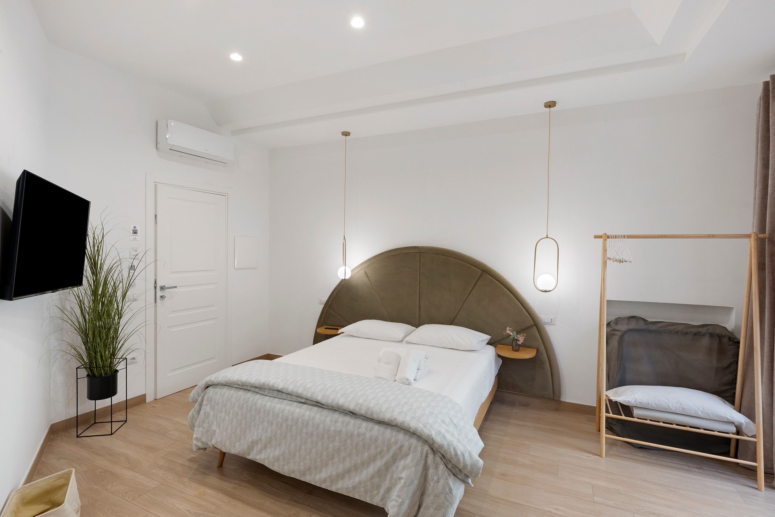 Een slaapkamer met een bed, nachtkastje, hanglamp en een aan de muur bevestigde televisie.