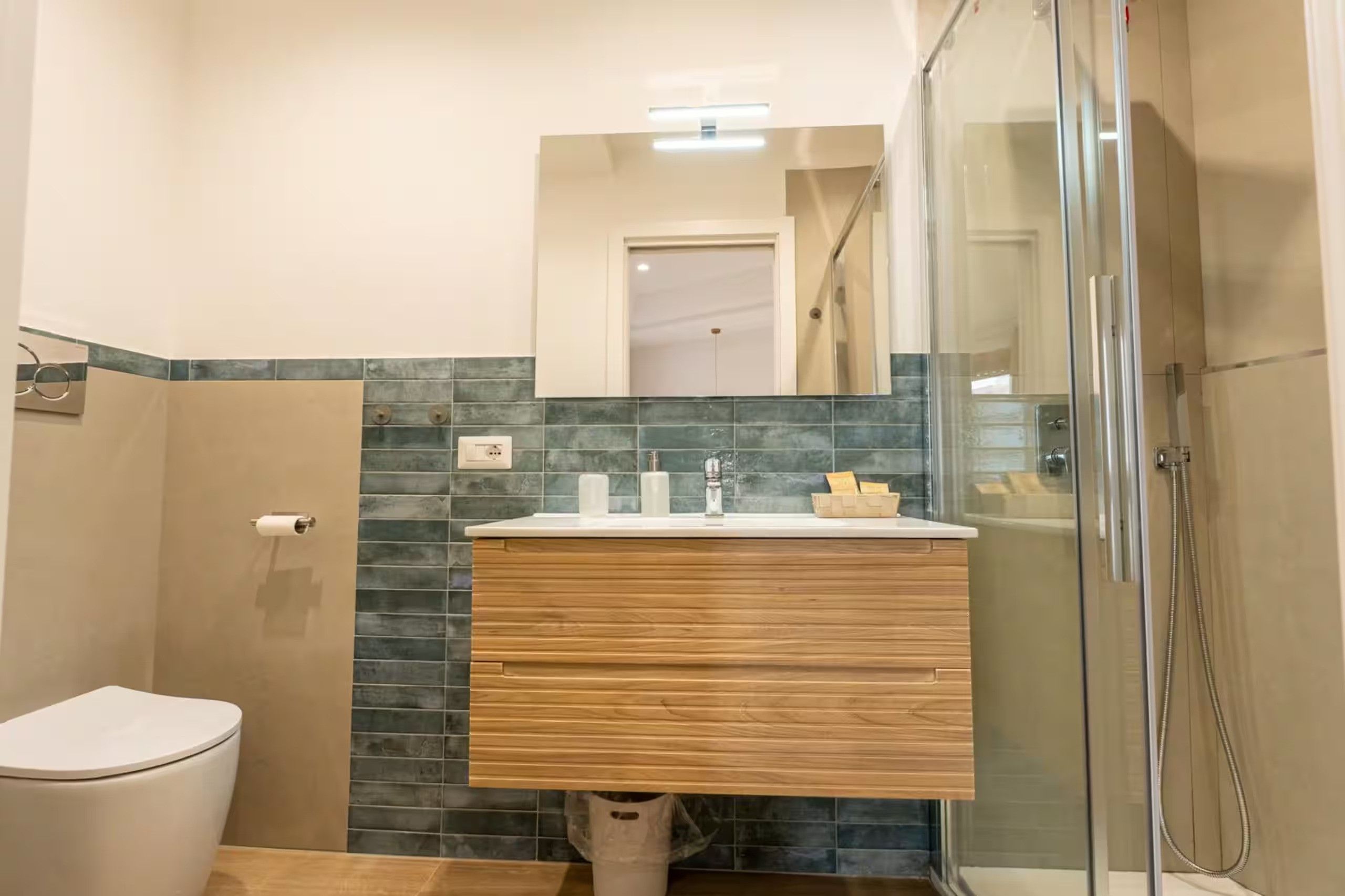 Ein Badezimmer mit Glasdusche, Holzwaschtisch und Spiegel sowie Toilette.