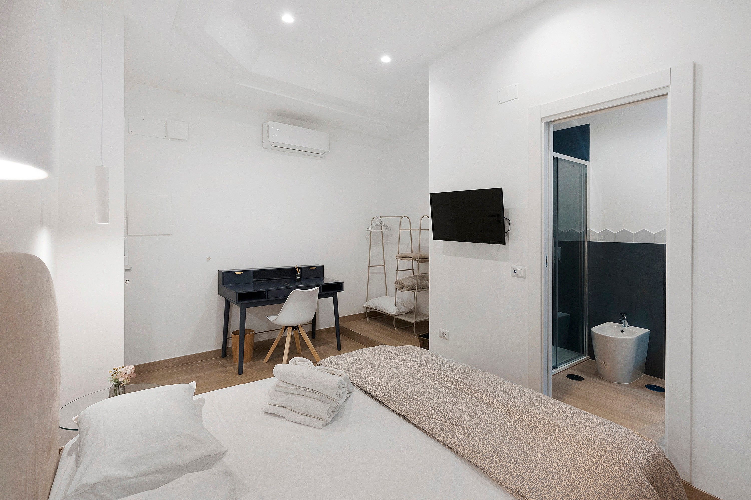 Een slaapkamer met een bed, een bureau, een stoel, een televisie en een badkamer met een wastafel en douche.