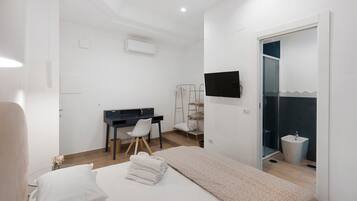 Een slaapkamer met een bed, een bureau, een stoel, een televisie en een badkamer met een wastafel en douche.