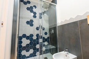 Een moderne badkamer met een douchecabine van glas, tegels met een honingraatpatroon en een wit wastafelmeubel.