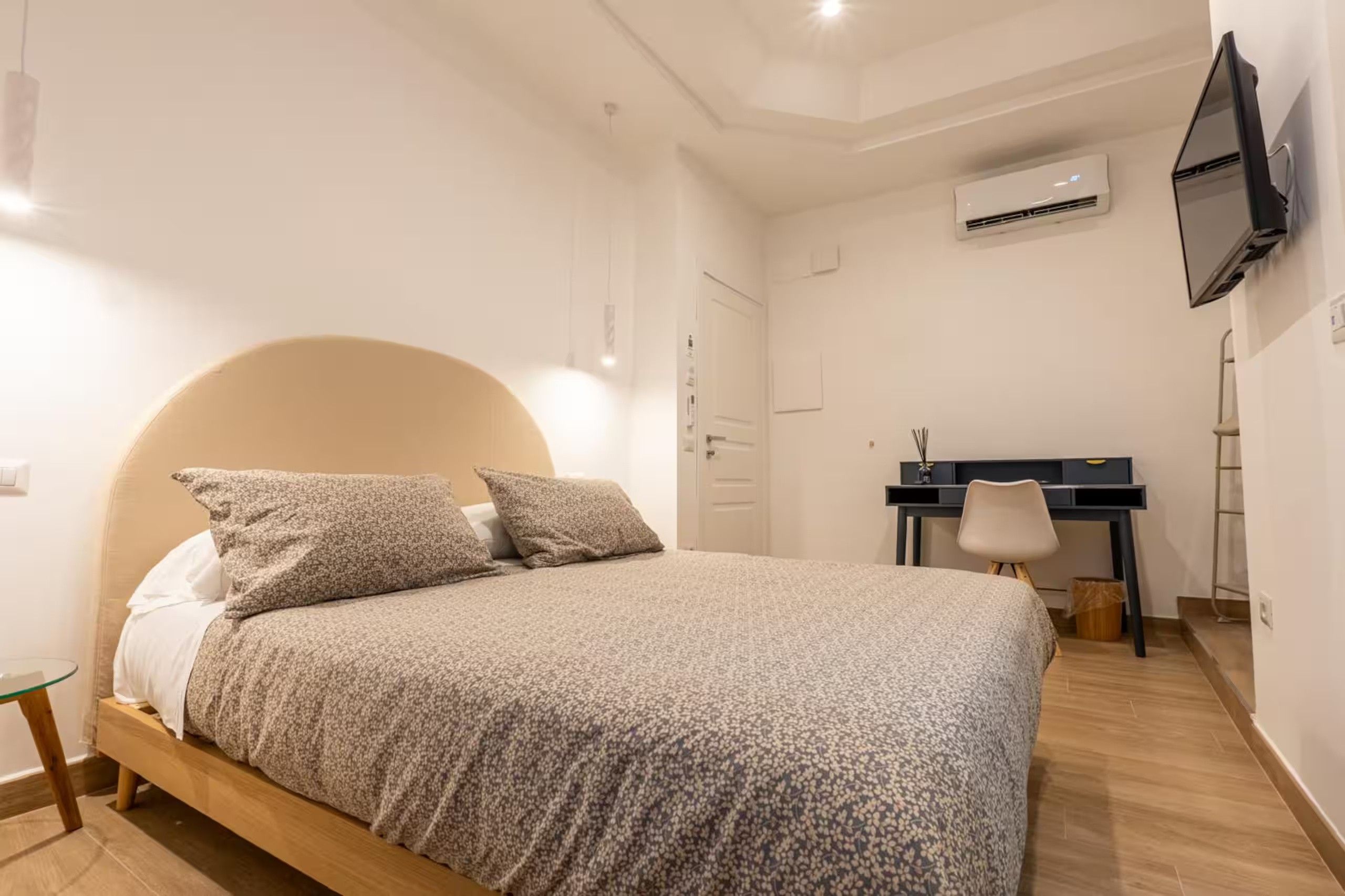 A bedroom with a bed, a desk, and an air conditioning unit.
