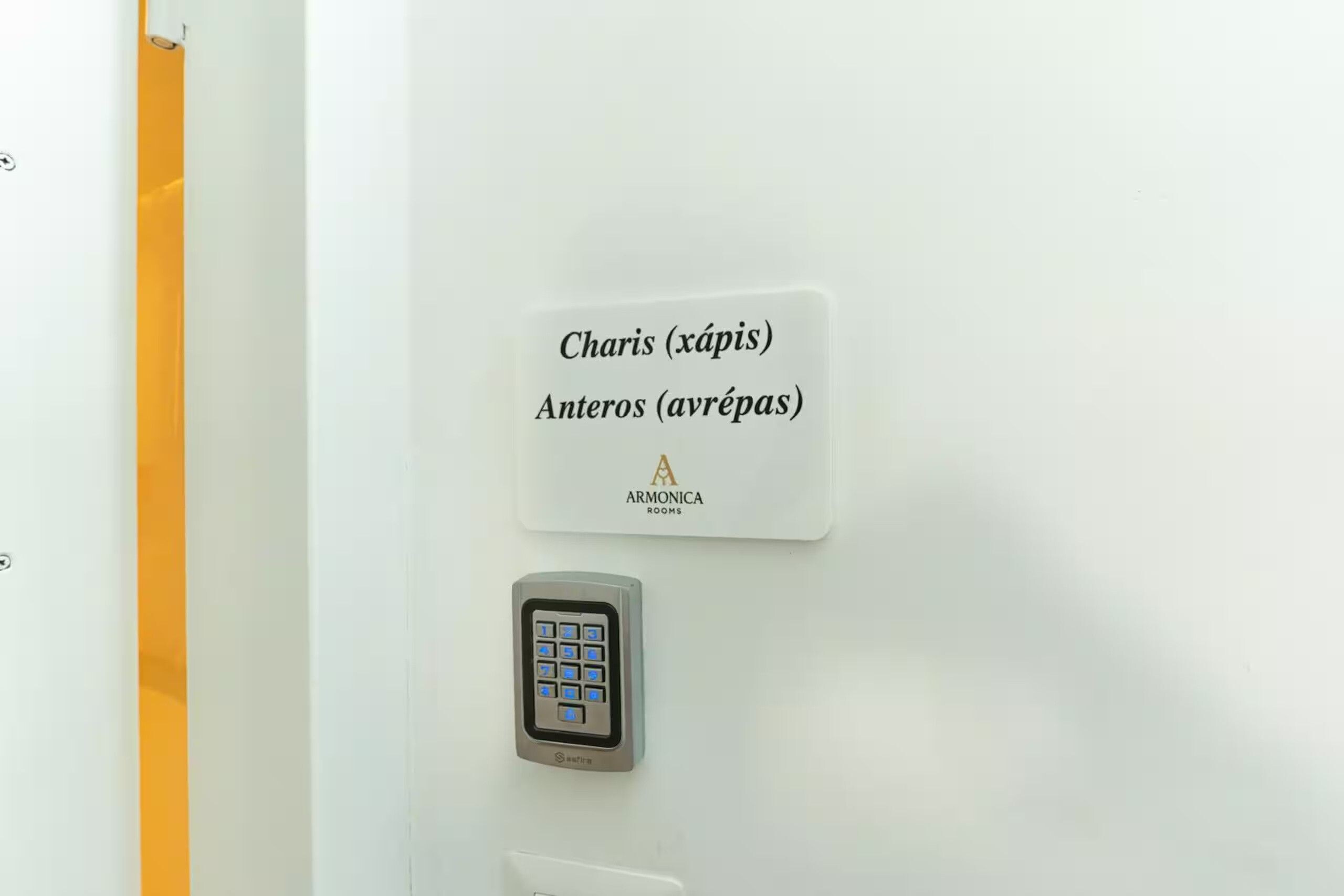 Una camera d'albergo con serratura a combinazione e un cartello che indica i numeri delle stanze 'Charis (xápis)' e 'Anteros (avrépas)'.