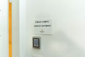 Quarto de hotel com fechadura por teclado numérico e placa indicando os números de quarto 'Charis (xápis)' e 'Anteros (avrépas)'.