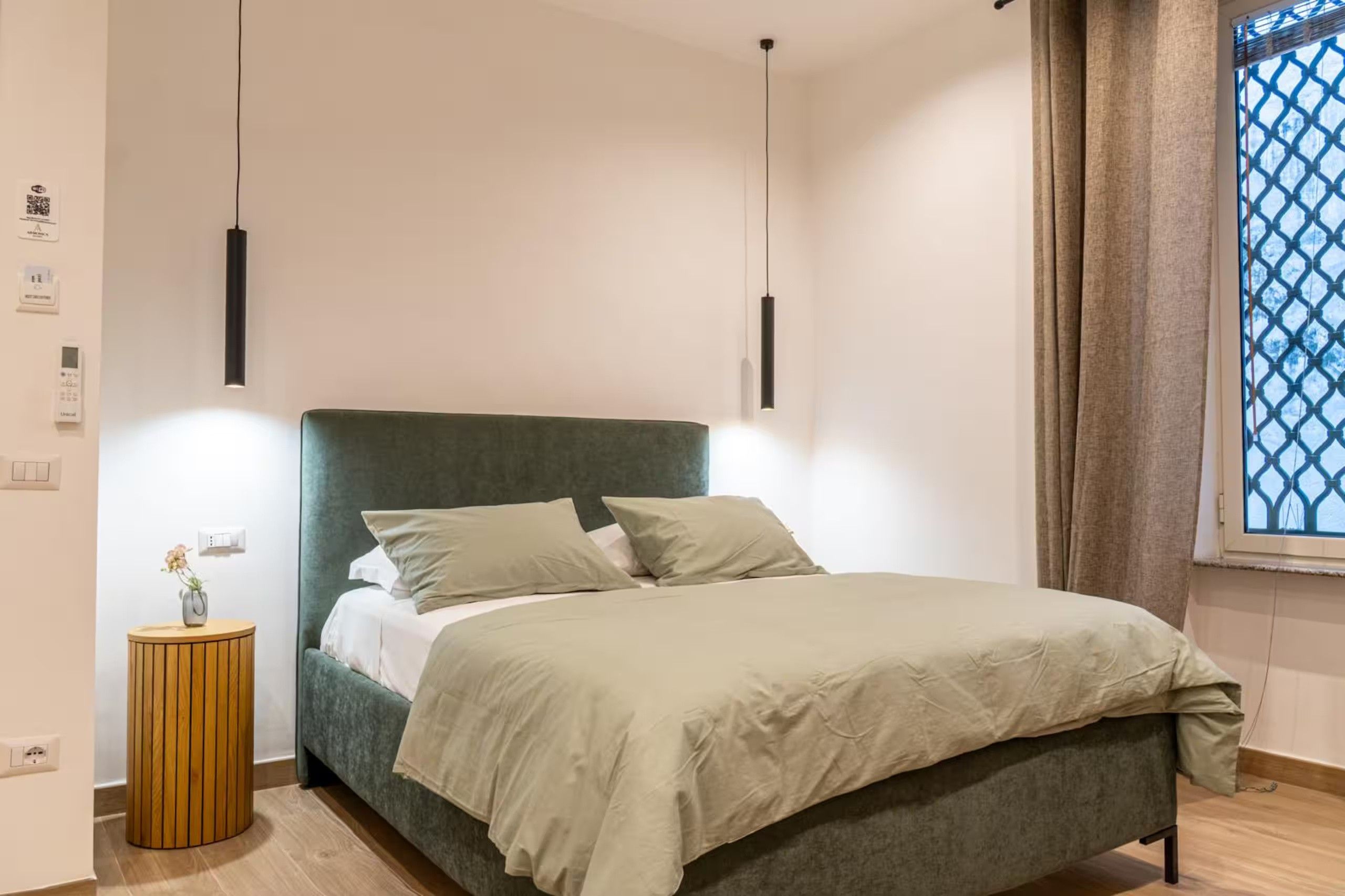 Ett modernt sovrum med en säng, sänglampor, ett litet träbord och ett fönster med utsikt.