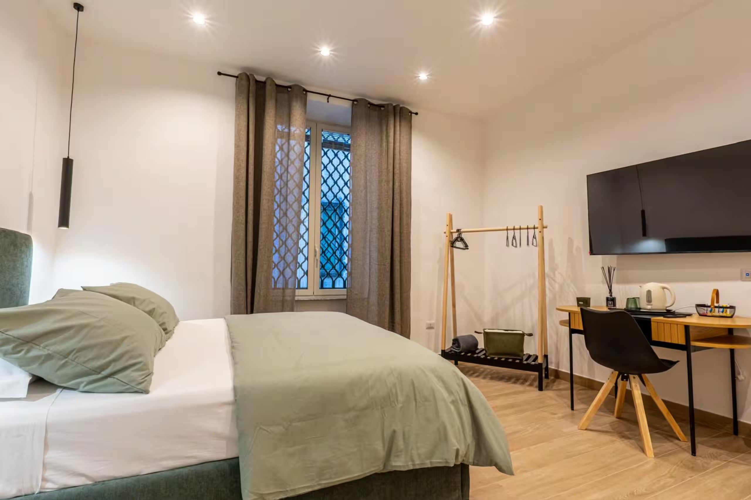 Ein Schlafzimmer mit Bett, Schreibtisch, Stuhl, Fernseher und einem Fenster mit Vorhängen.