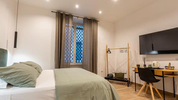 Ein Schlafzimmer mit Bett, Schreibtisch, Stuhl, Fernseher und einem Fenster mit Vorhängen.