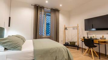 Ein Schlafzimmer mit Bett, Schreibtisch, Stuhl, Fernseher und einem Fenster mit Vorhängen.