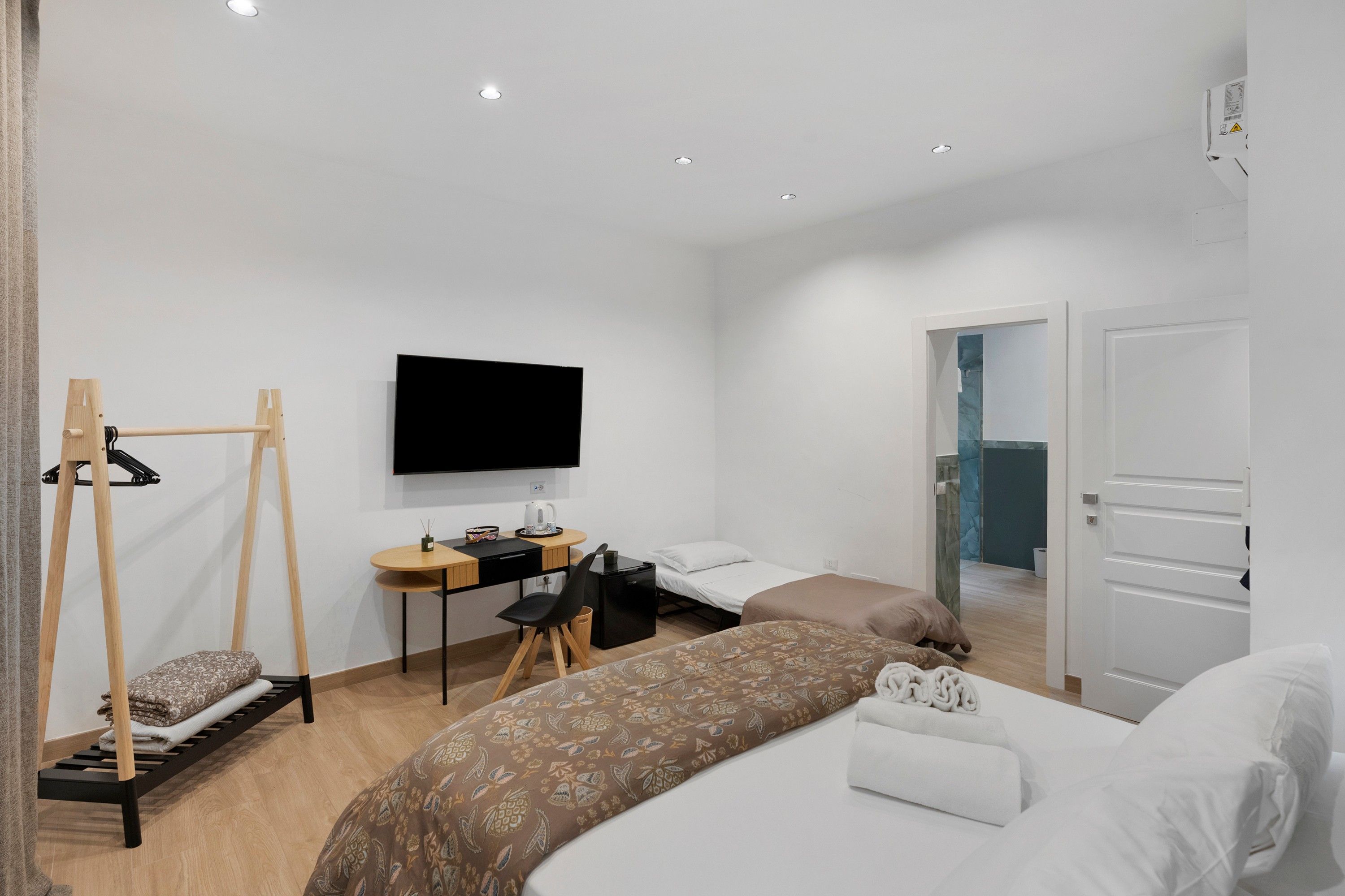 Et moderne hotelværelse med seng, skrivebord, stol, fjernsyn og garderobeskab.