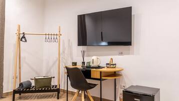 A compact room with a bed, a desk, a chair, a TV, and a small kitchenette.