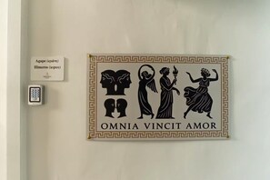 Un muro con un cartello decorativo raffigurante figure classiche e la frase 'OMNIA VINCIT AMOR'.