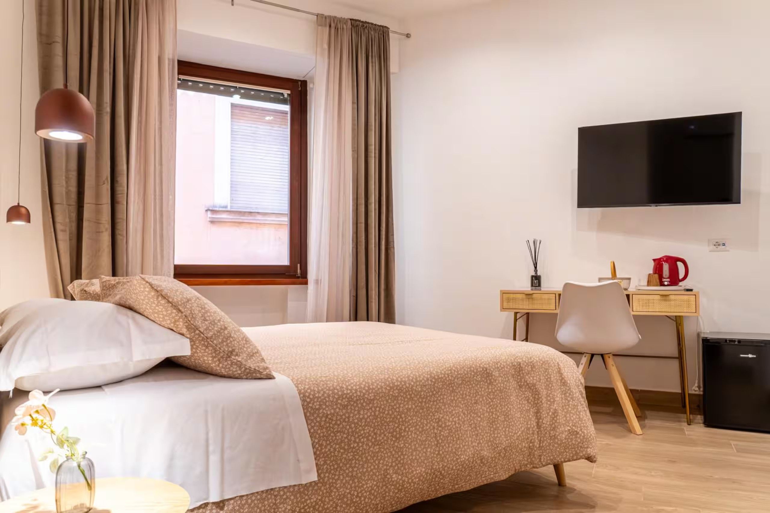 A hotel room with a bed, a desk, a television, and a window with curtains.