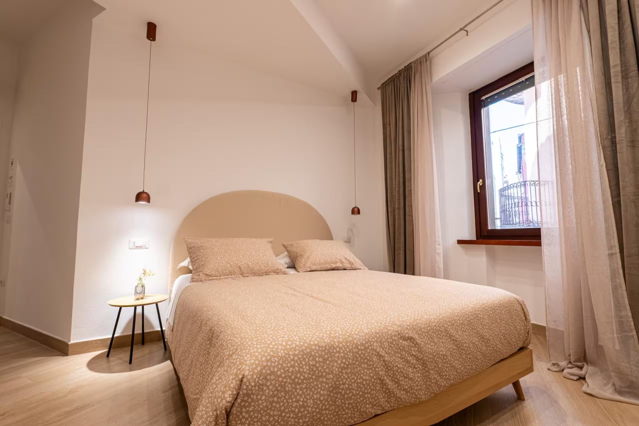 Una camera da letto con un letto, un comodino, una finestra con tende e vista sull'esterno.