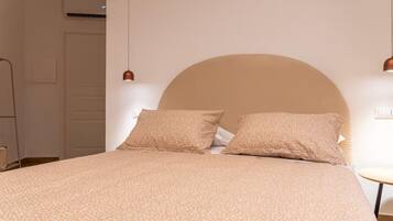 A bed with a large headboard, two pillows, and a patterned bedspread in a room with a white wall and a small table.