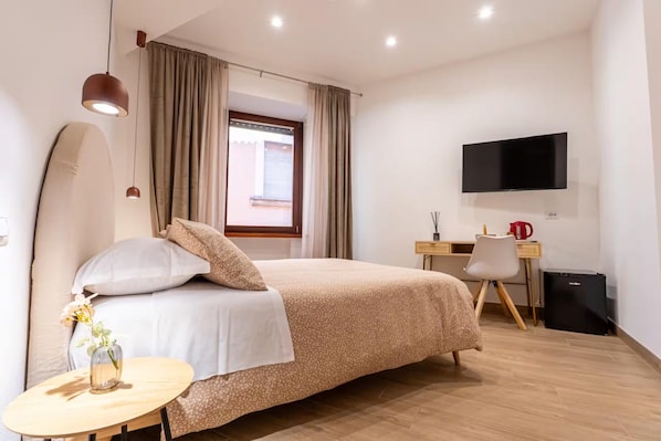 Una camera d'albergo con un letto, una scrivania, una sedia, un televisore e un tavolino con un vaso.