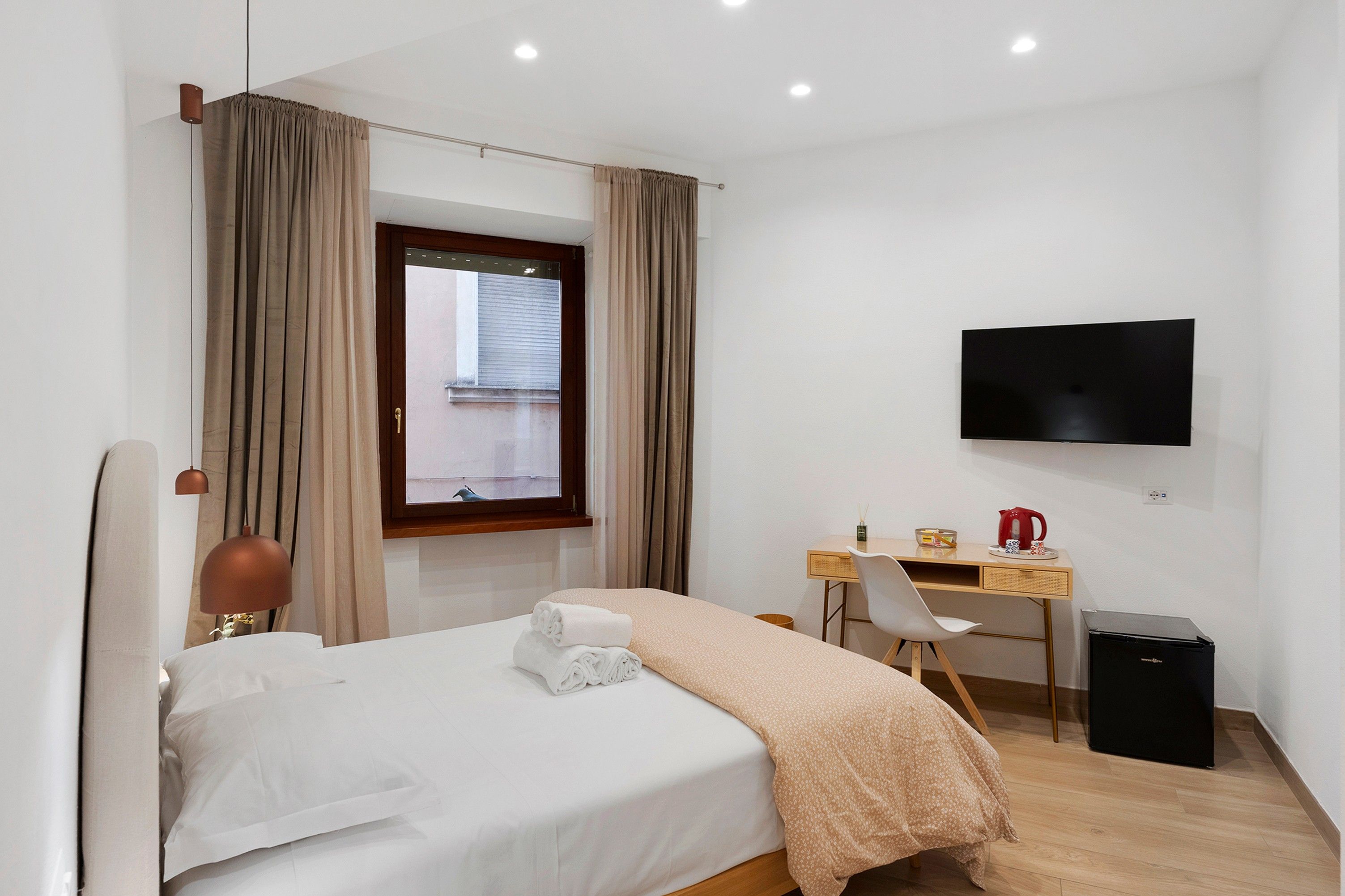 Una camera d'albergo con un letto, una scrivania, una sedia, una televisione e una finestra con tende.