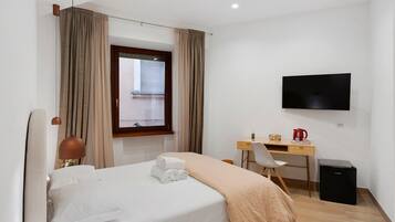 Una camera d'albergo con un letto, una scrivania, una sedia, una televisione e una finestra con tende.