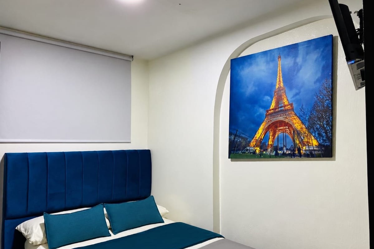 A bedroom with a bed, a headboard, and a painting of the Eiffel Tower.